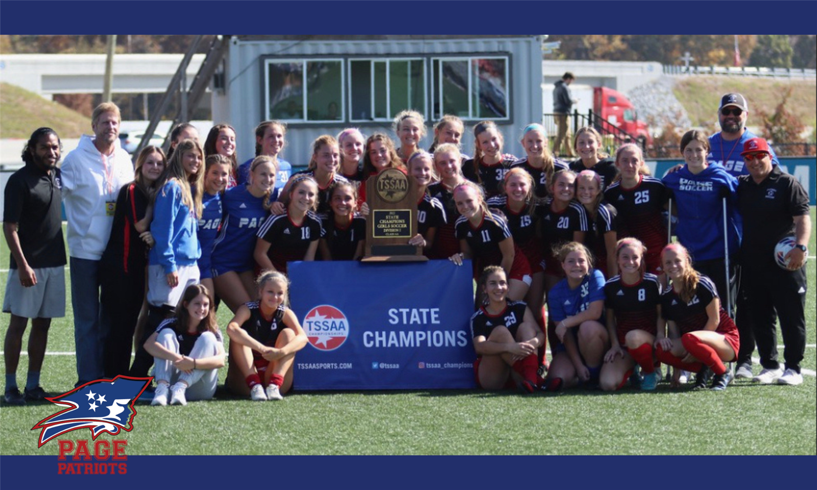 A soccer team sits with a championship banner